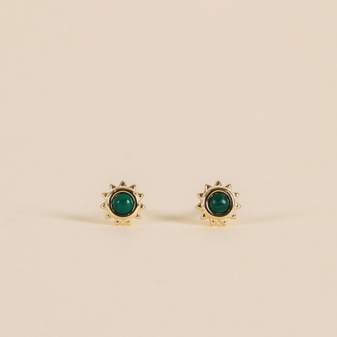 Gold earrings with green gemstones on a beige background