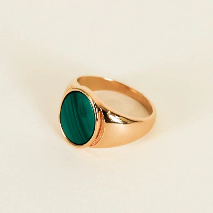 Gold ring with a green stone on a beige background