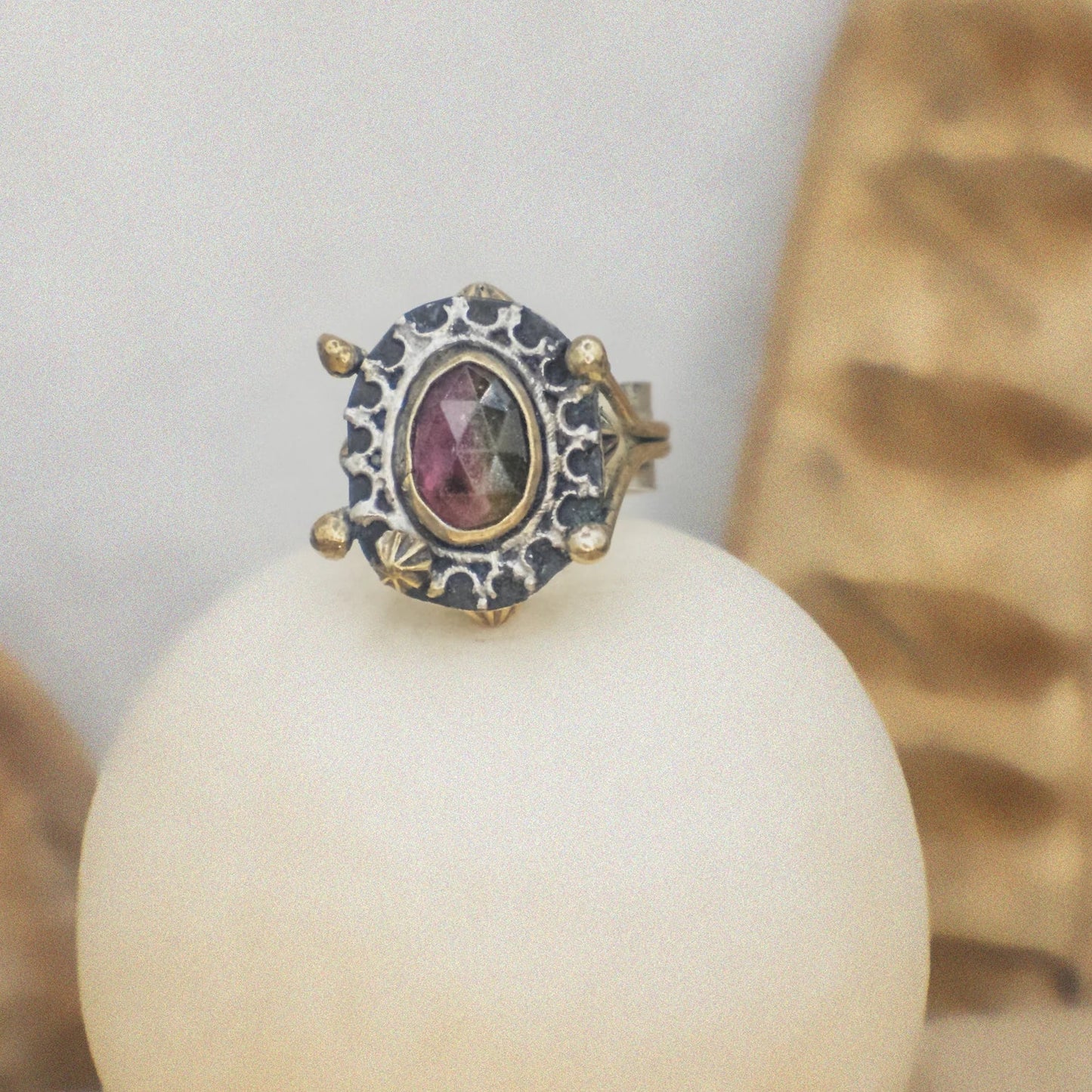 Ring with a gemstone on a white sphere against a neutral background
