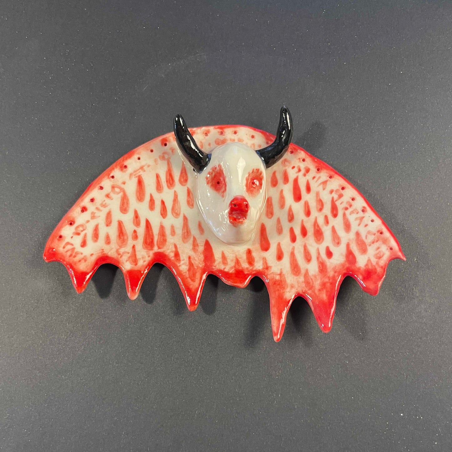 Bat-shaped object with red and white design on a gray background