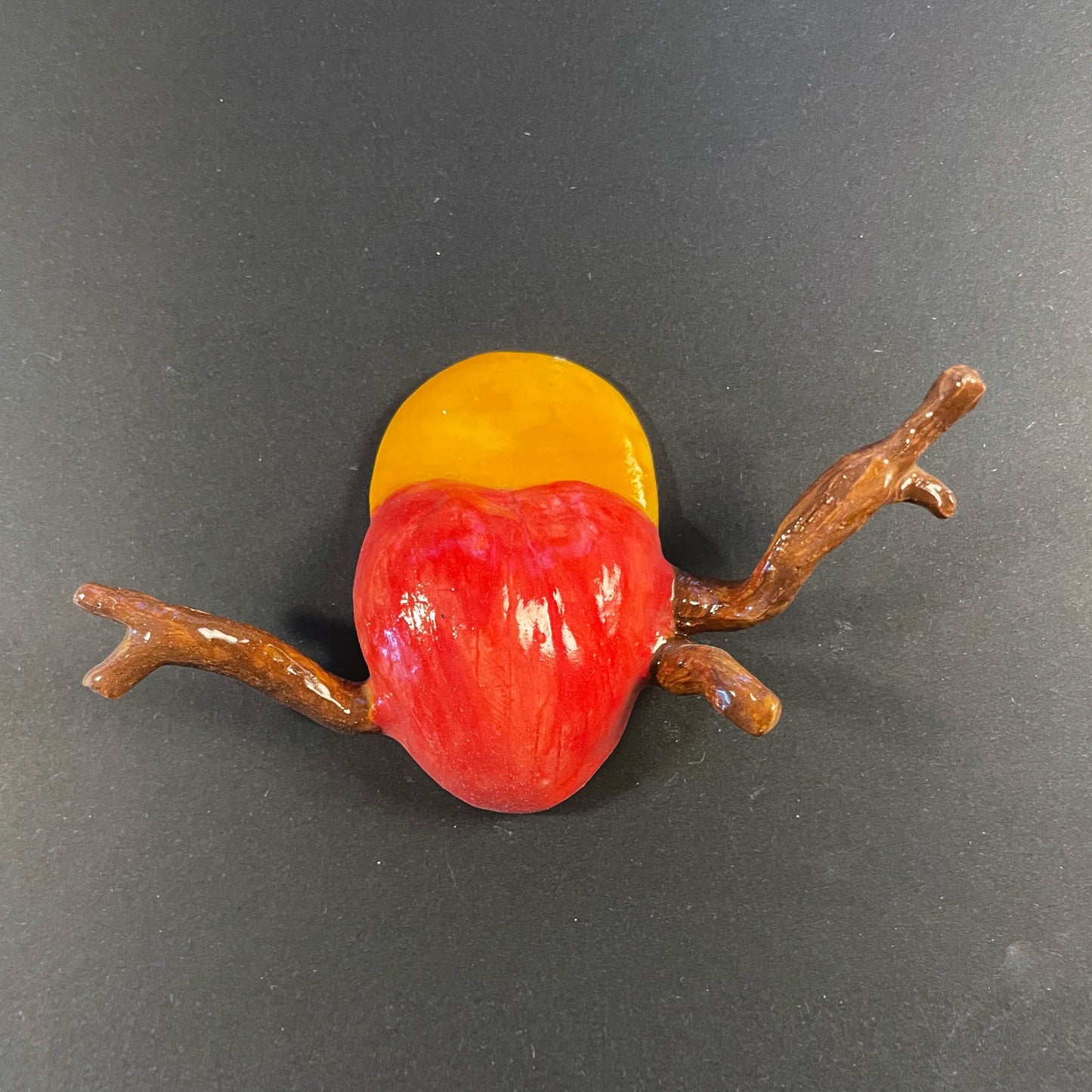 Decorative item resembling a red and yellow fruit with a branch on a dark background
