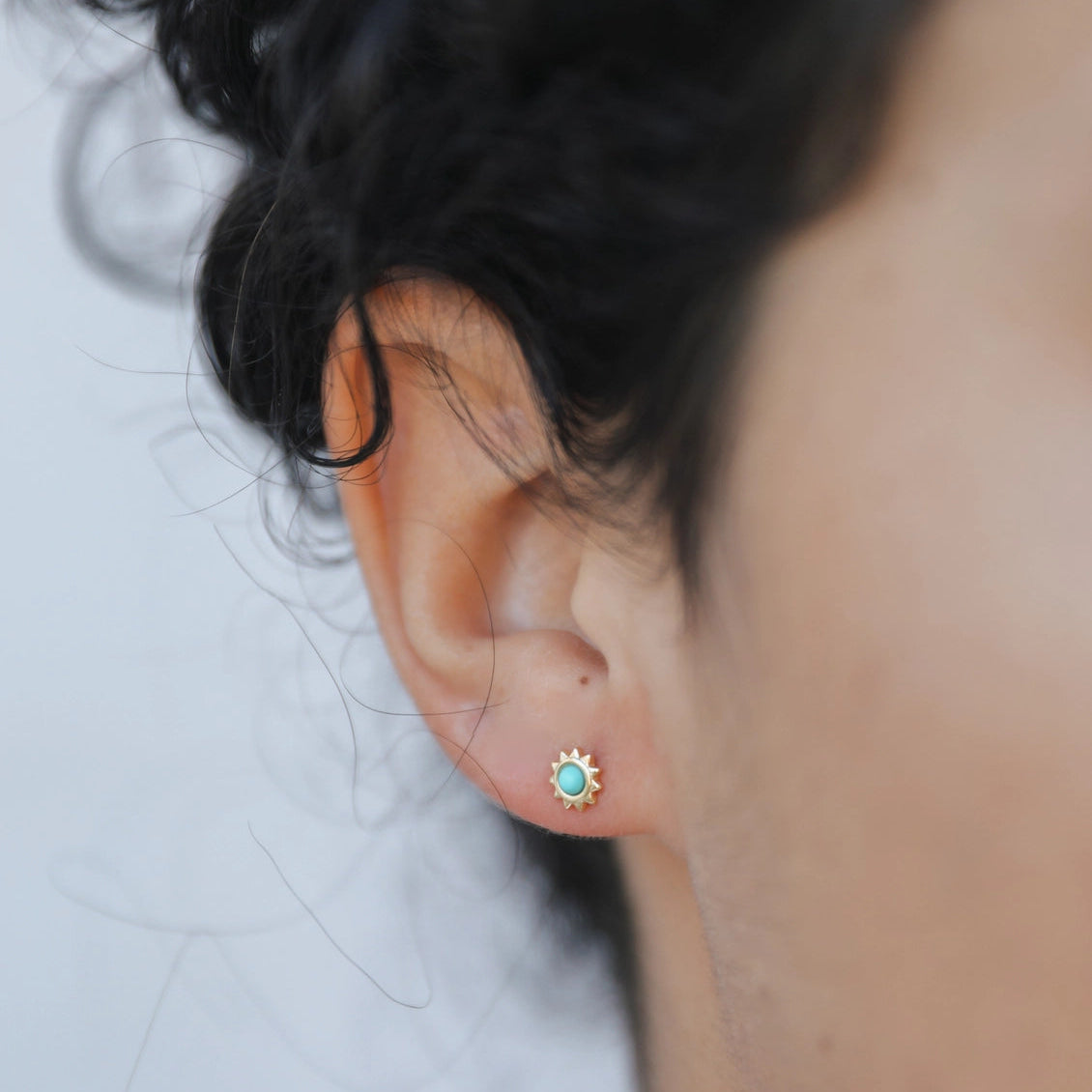 Close-up of an ear wearing a turquoise stud earring with a blurred background