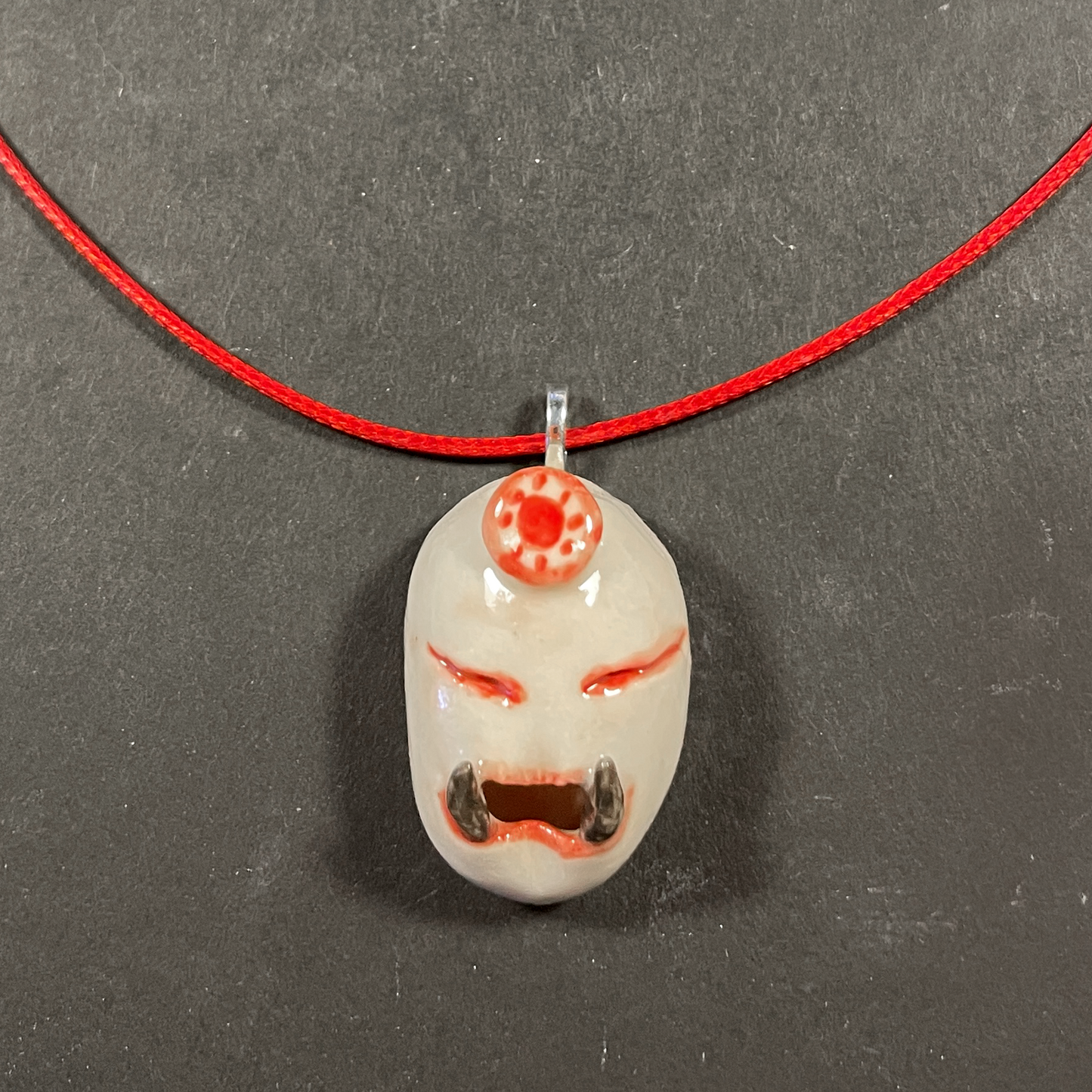 A handmade ceramic pendant on a red cord necklace, displayed on a dark gray textured background.