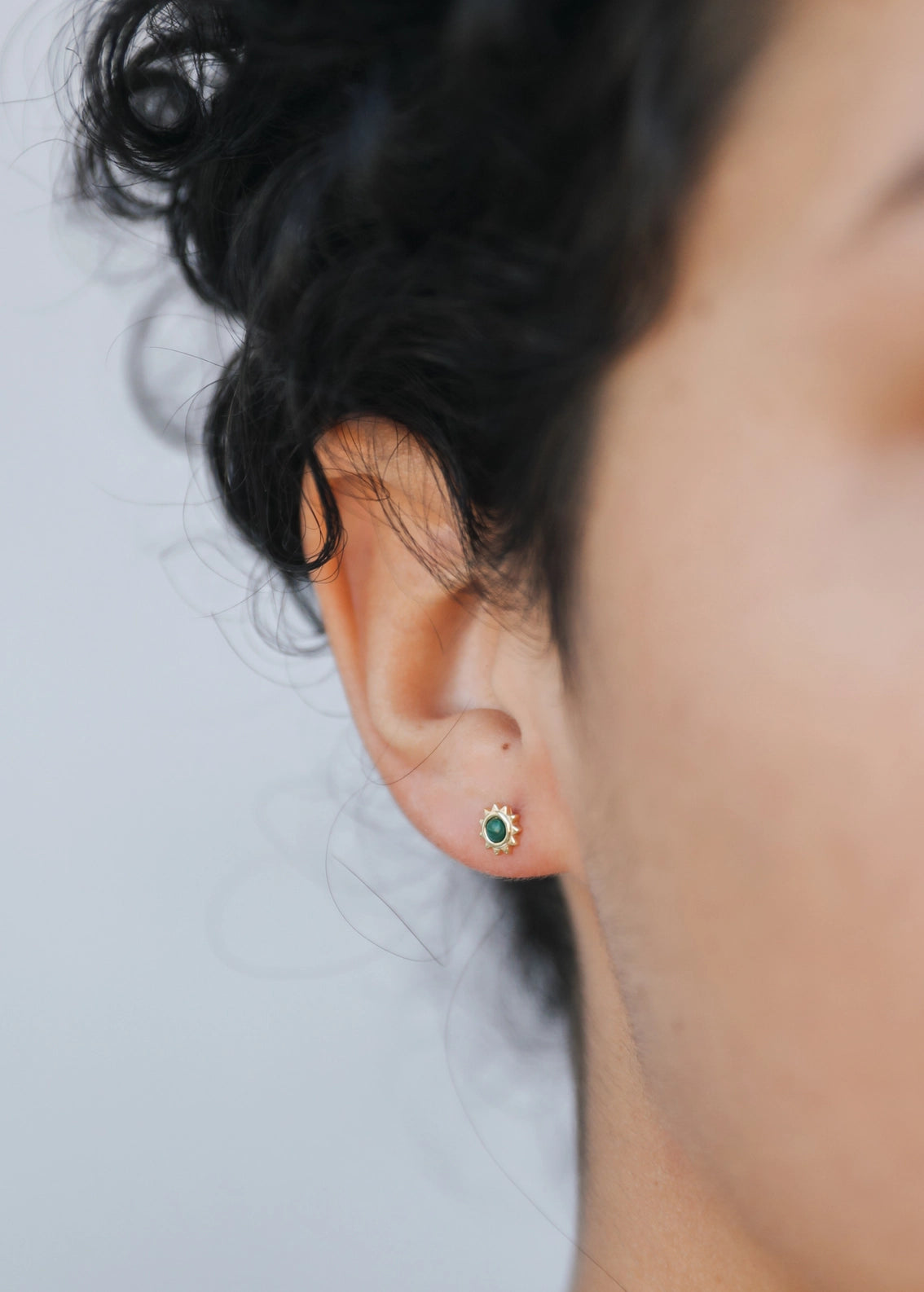 Close-up of an ear wearing a green gemstone earring with a blurred background