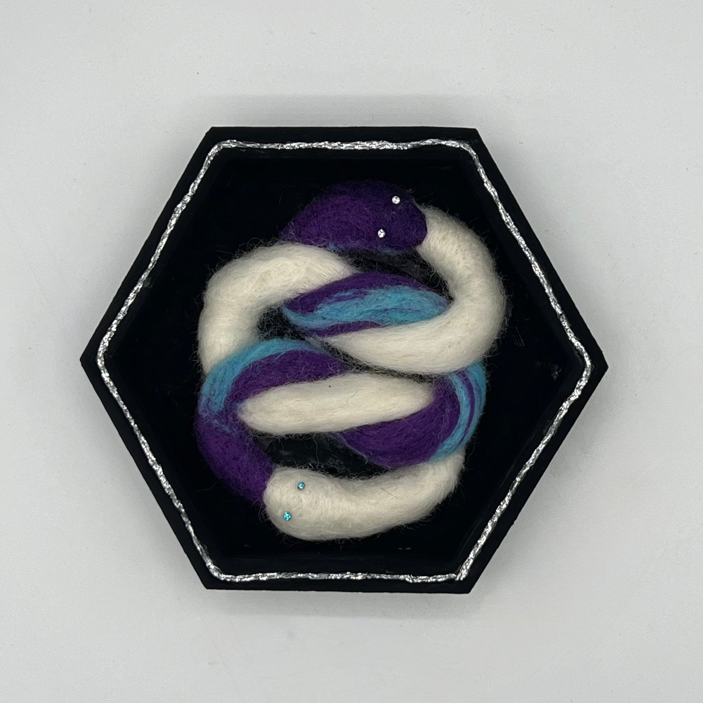 Hexagonal brooch with intertwined white and purple snake on a light gray background