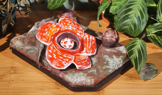 Decorative red and orange ceramic flower on a stone base with green leaves in the background