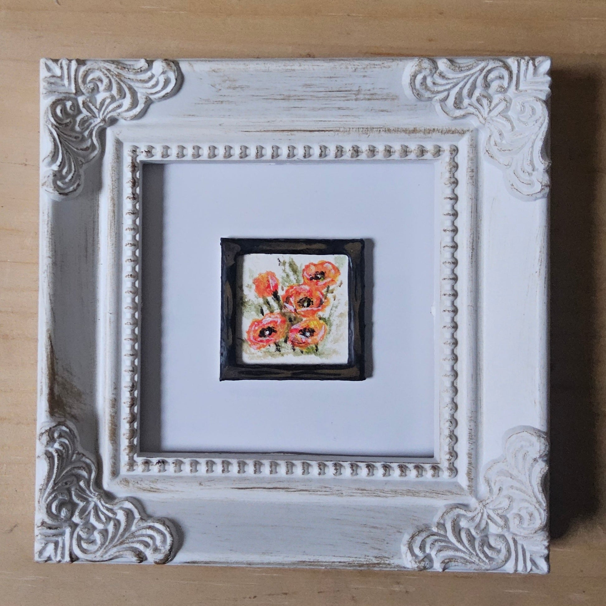 Decorative white frame with a small floral painting inside on a wooden surface
