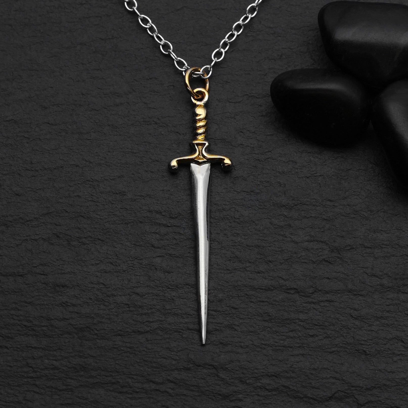 Silver dagger pendant on a chain against a dark background