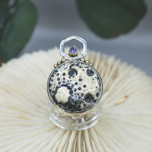 Close-up of a decorative ring on a textured surface with blurred green leaves in the background