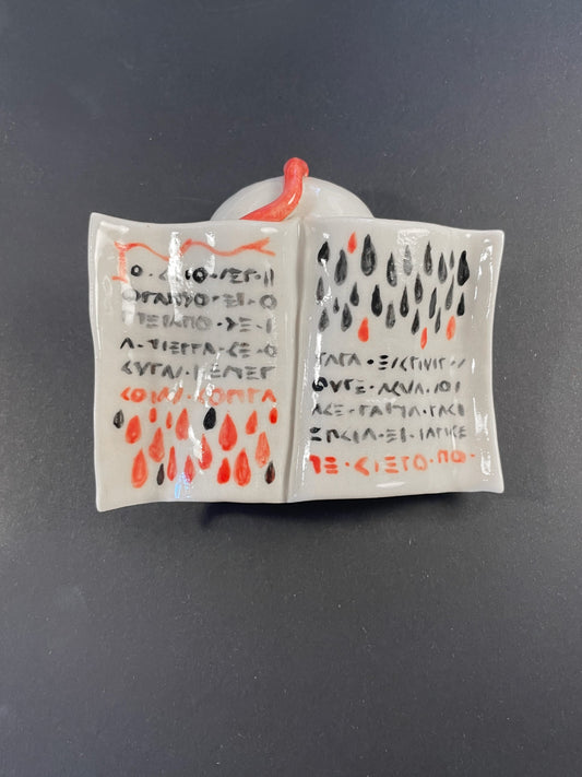Small ceramic book with painted text and symbols on a dark background