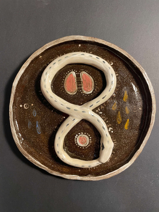Ceramic plate with a white snake design on a dark background