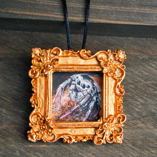 Decorative gold frame with a small painting of a spider on a dark surface