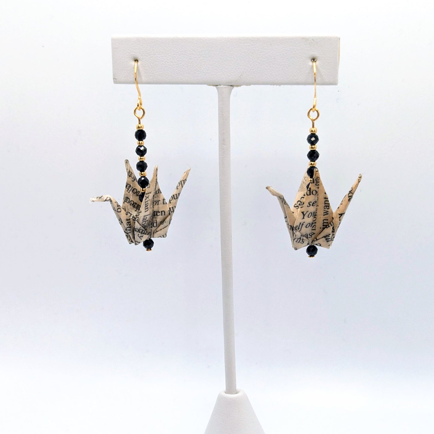 Pair of earrings with paper crane design on a white stand against a white background