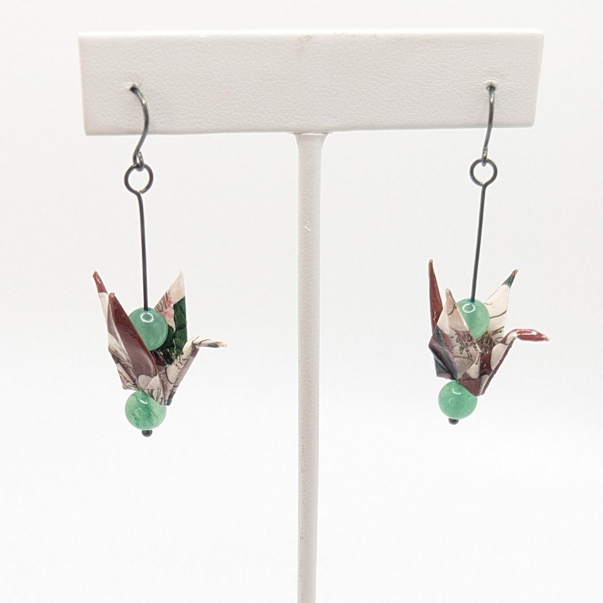 Pair of origami bird earrings on a white stand with a white background