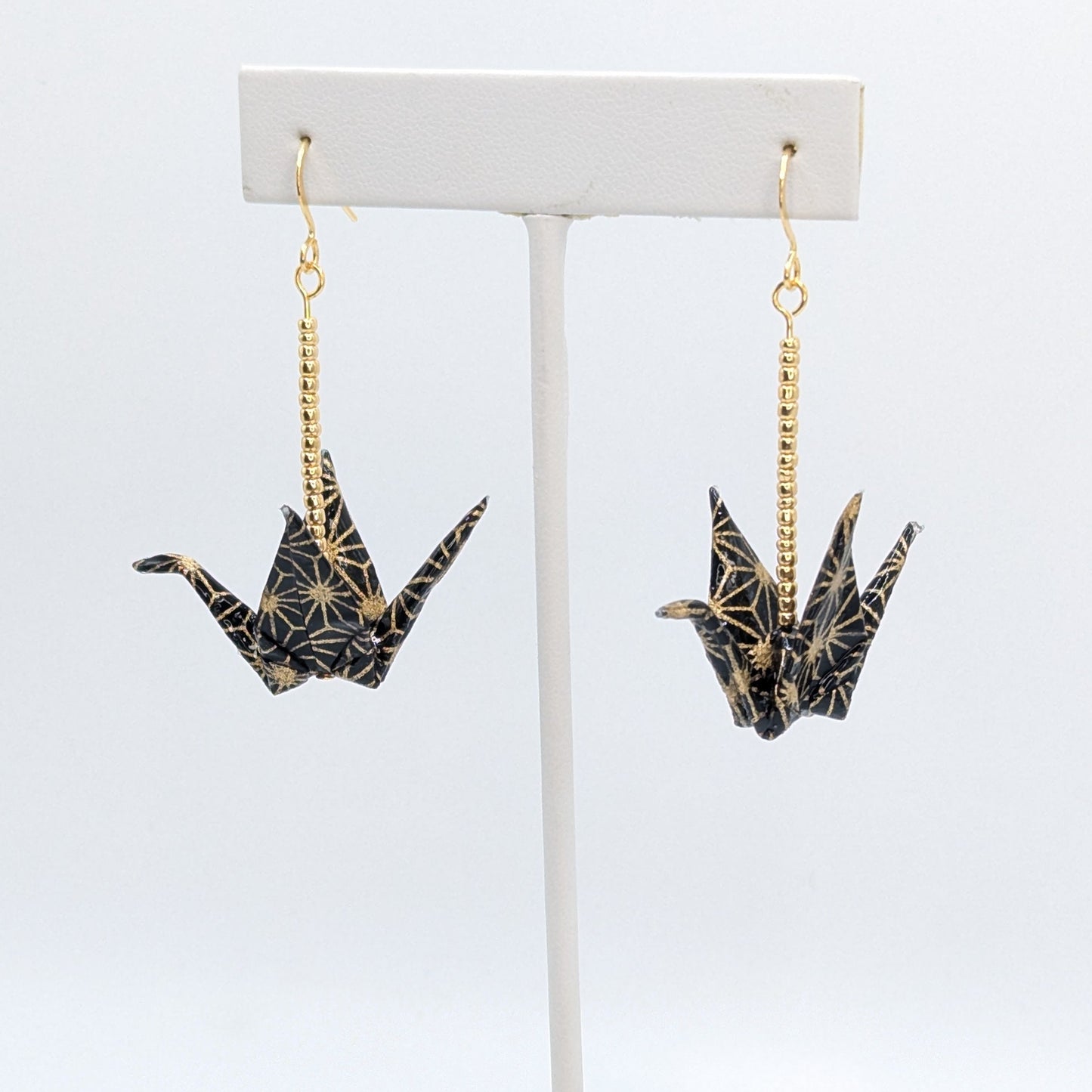 Pair of crane-shaped earrings on a white stand with a white background