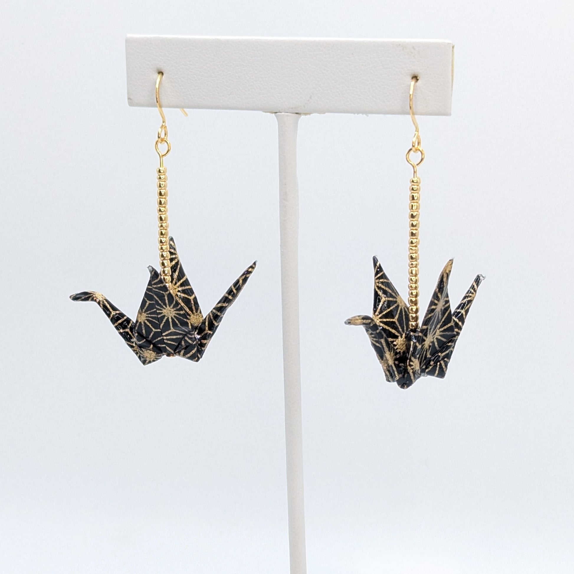 Pair of crane-shaped earrings on a white stand with a white background
