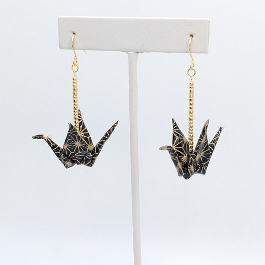 Pair of crane-shaped earrings on a white stand with a white background