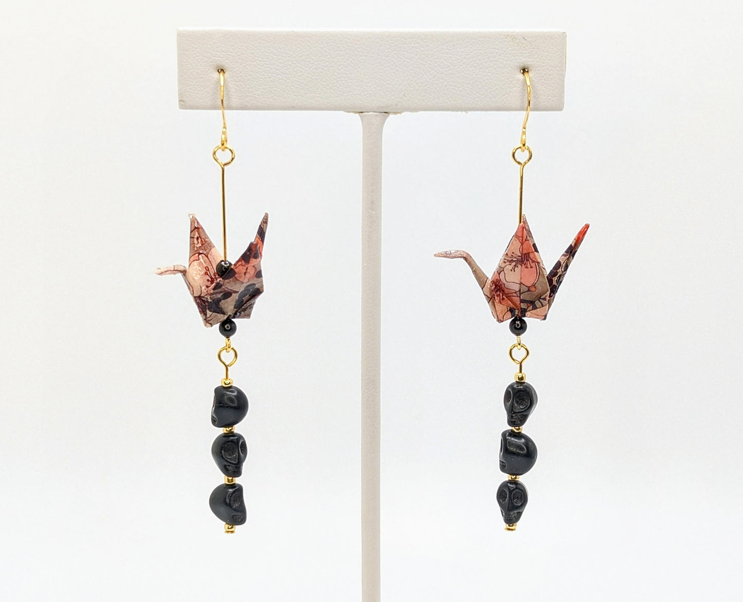 Pair of origami crane earrings with black beads on a white background