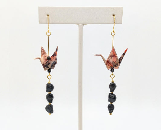Pair of origami crane earrings with black beads on a white background