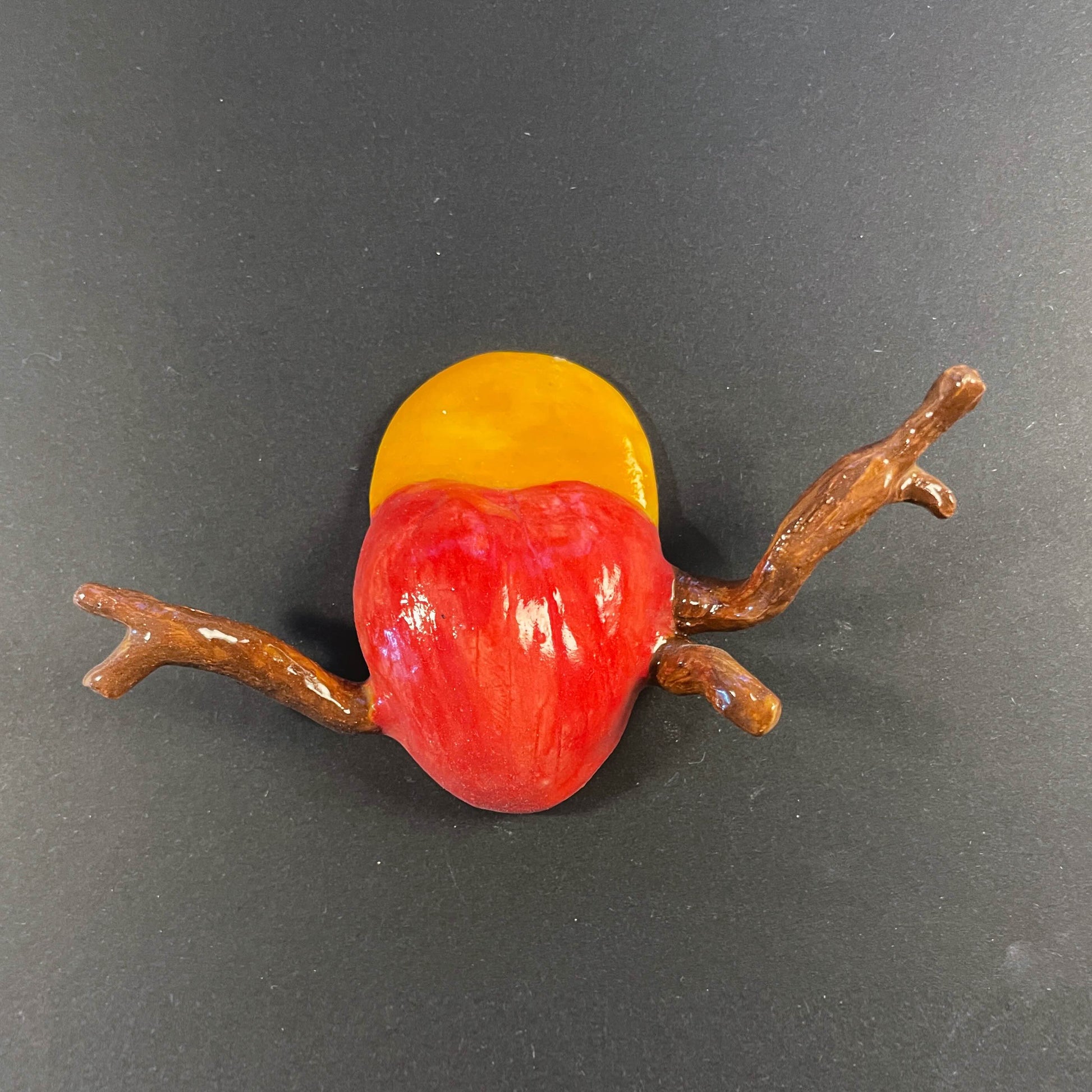 Decorative item resembling a red and yellow fruit with a branch on a dark background