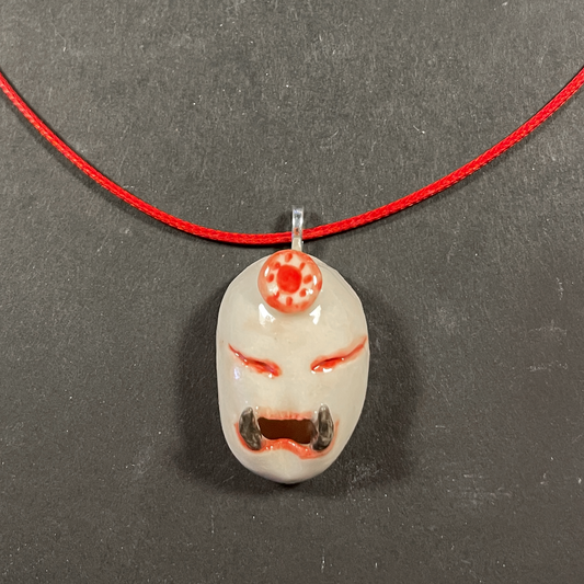 A handmade ceramic pendant on a red cord necklace, displayed on a dark gray textured background.