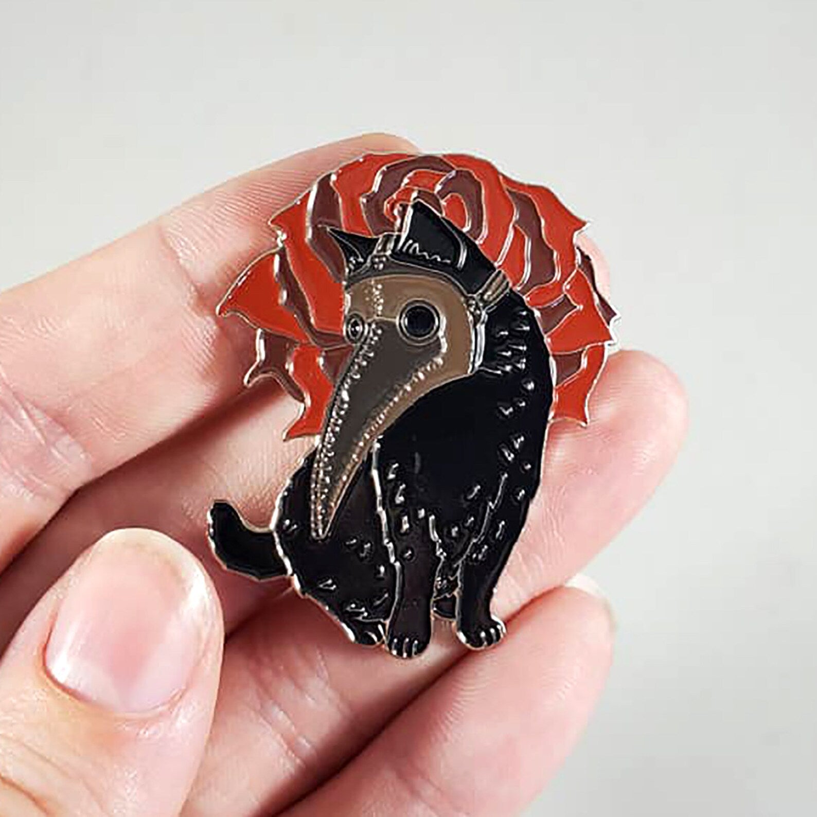 Black cat with red rose pin held in a hand against a light gray background