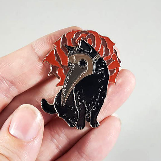 Black cat with red rose pin held in a hand against a light gray background