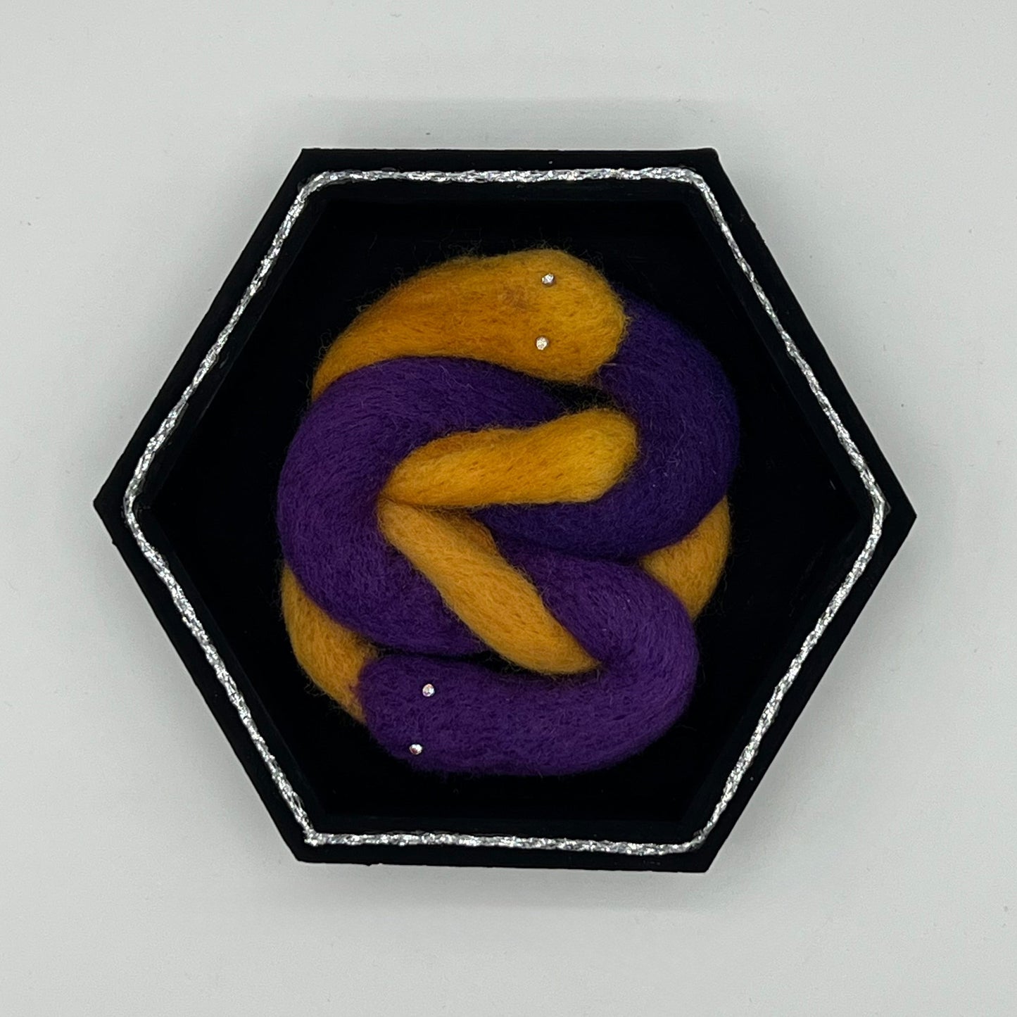 Hexagonal brooch with purple and gold knot design on a light gray background