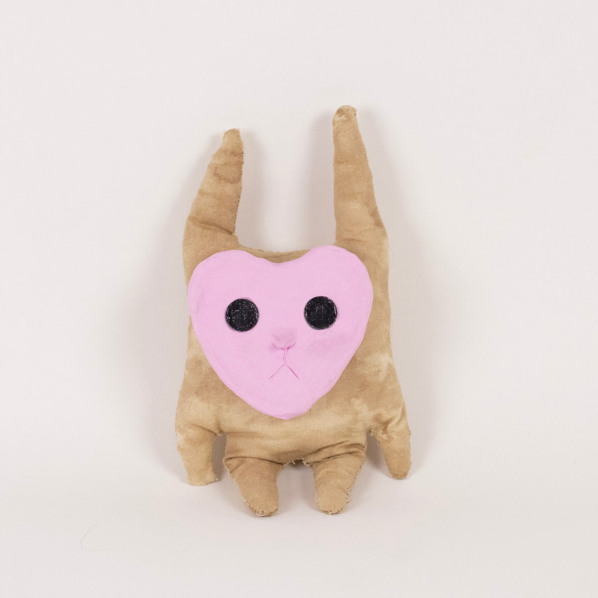 A small plush toy shaped like a tan creature with long pointed ears and a pink heart-shaped face with black embroidered eyes, centered on a plain white background.