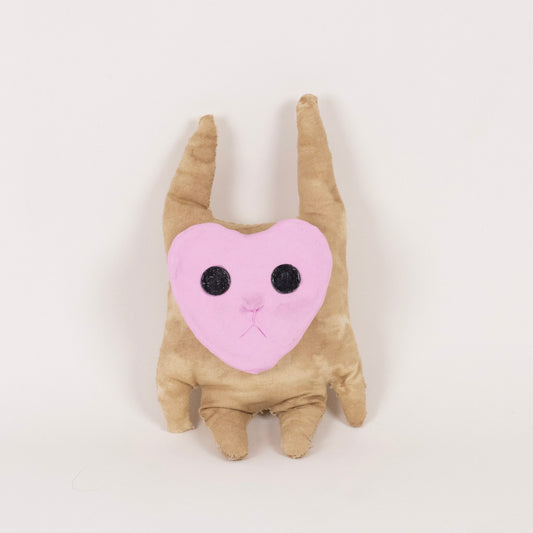A small plush toy shaped like a tan creature with long pointed ears and a pink heart-shaped face with black embroidered eyes, centered on a plain white background.
